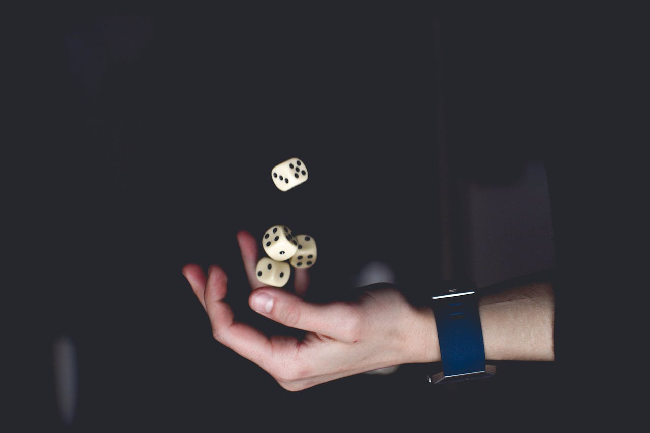 heros-img A close-up of a hand tossing several dice against a dark background, symbolizing chance and luck.